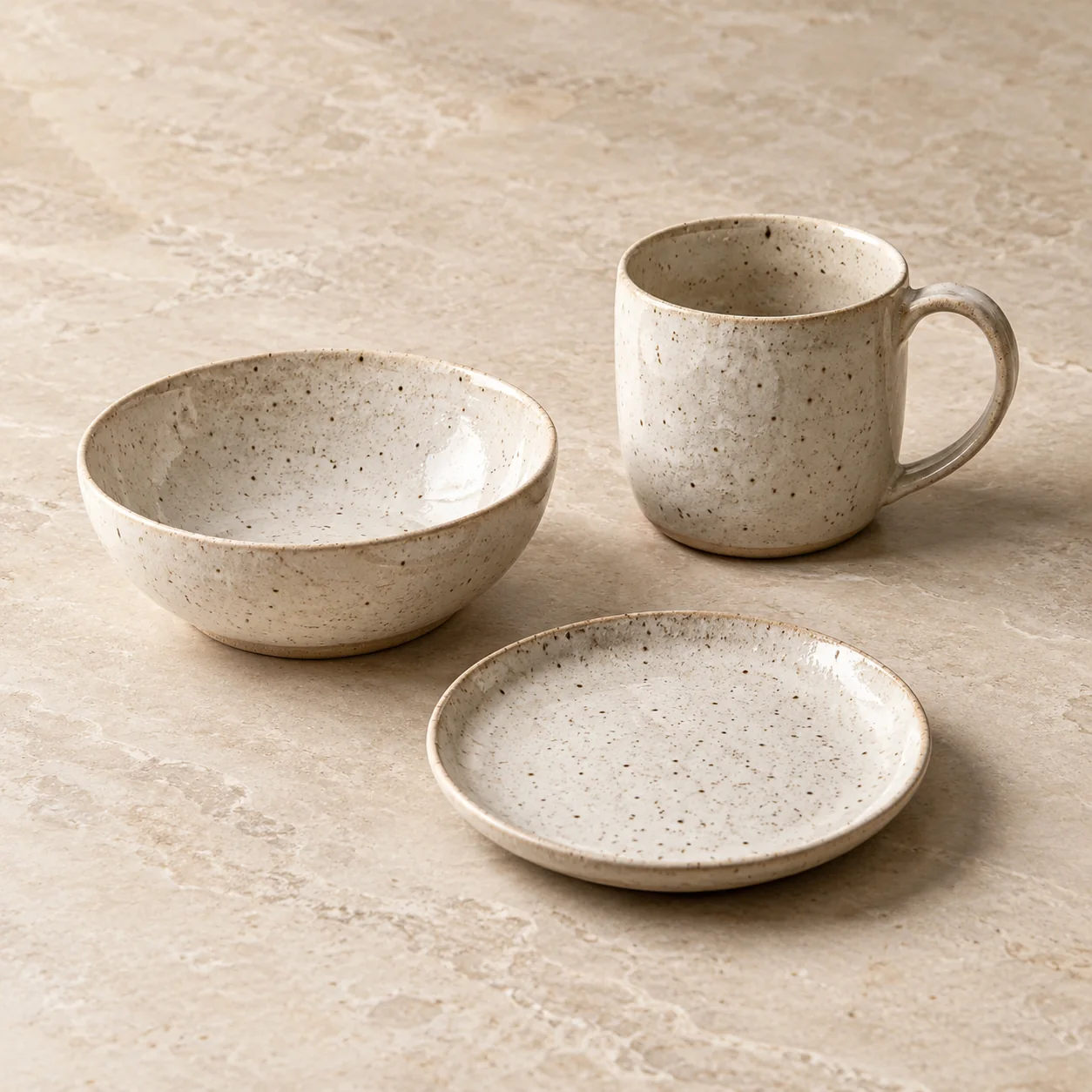 Editorial concept with exactly three speckled ceramic pieces: a mug, bowl and side plate